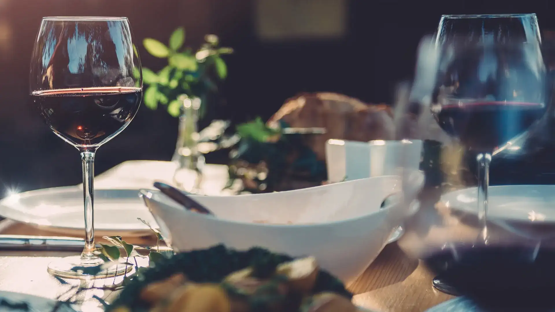 Dining table with glasses of red wine and place settings.