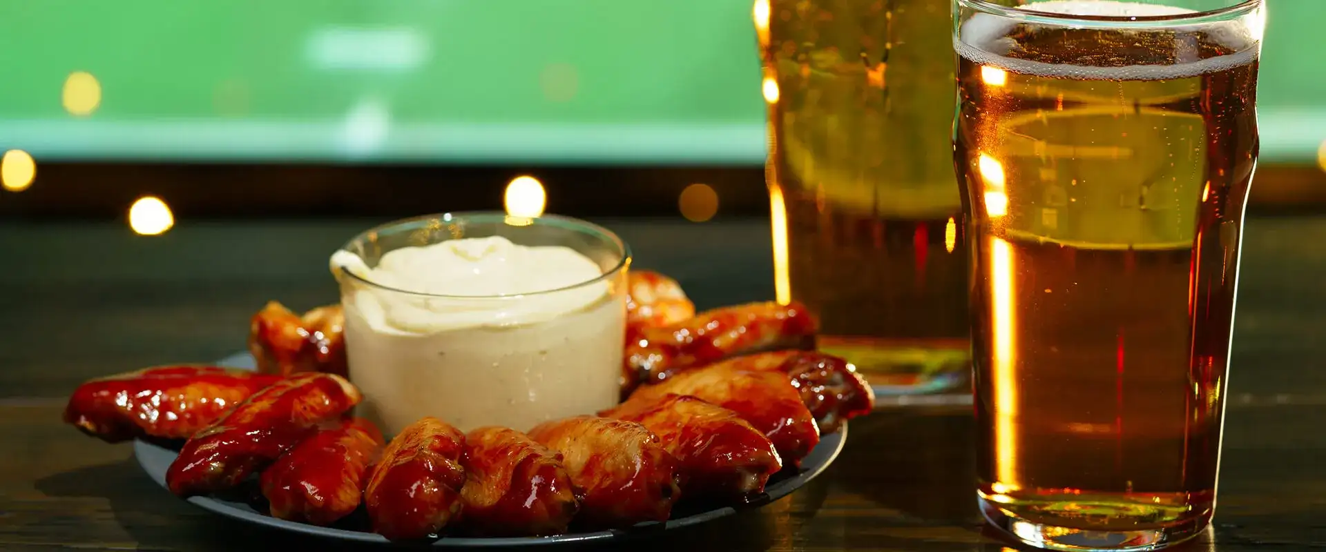 Chicken wings and glasses of beer in front of a football game on a TV