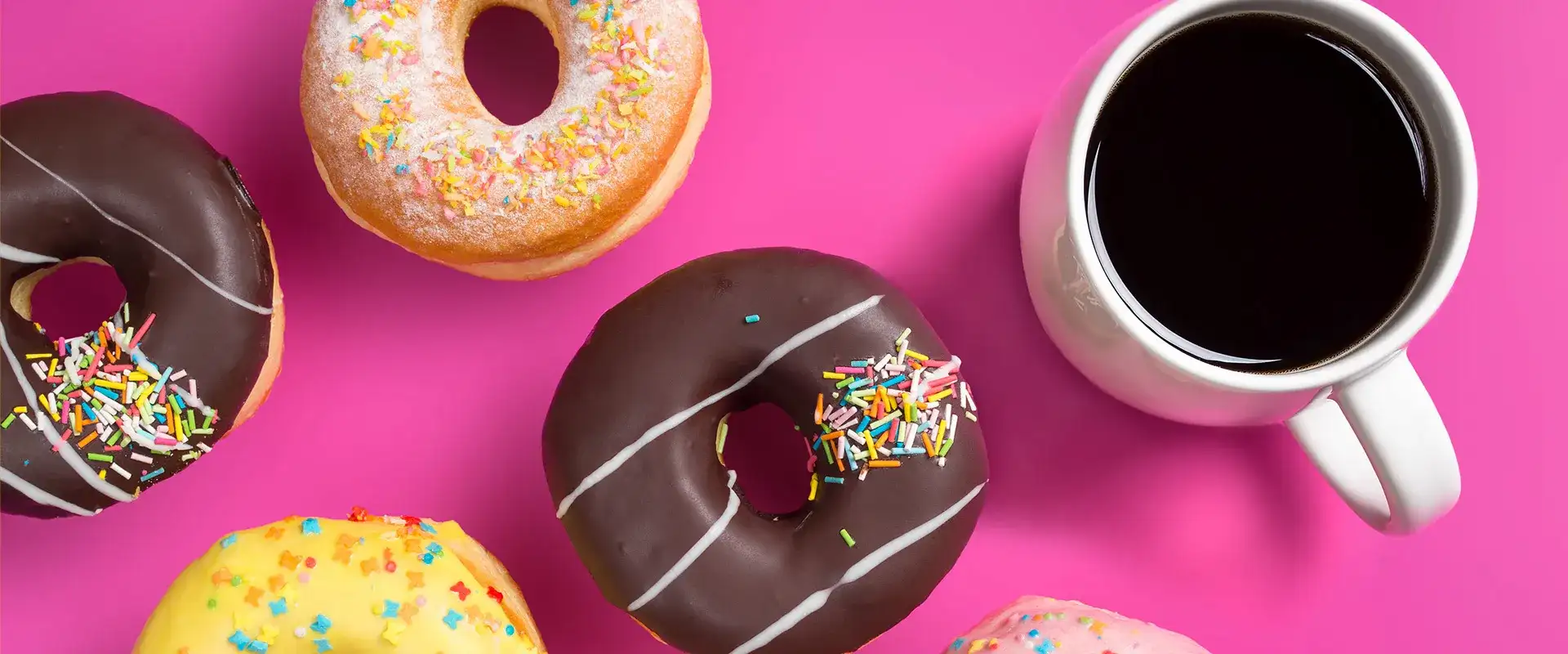 Donuts and mugs of coffee on a hot pink background.