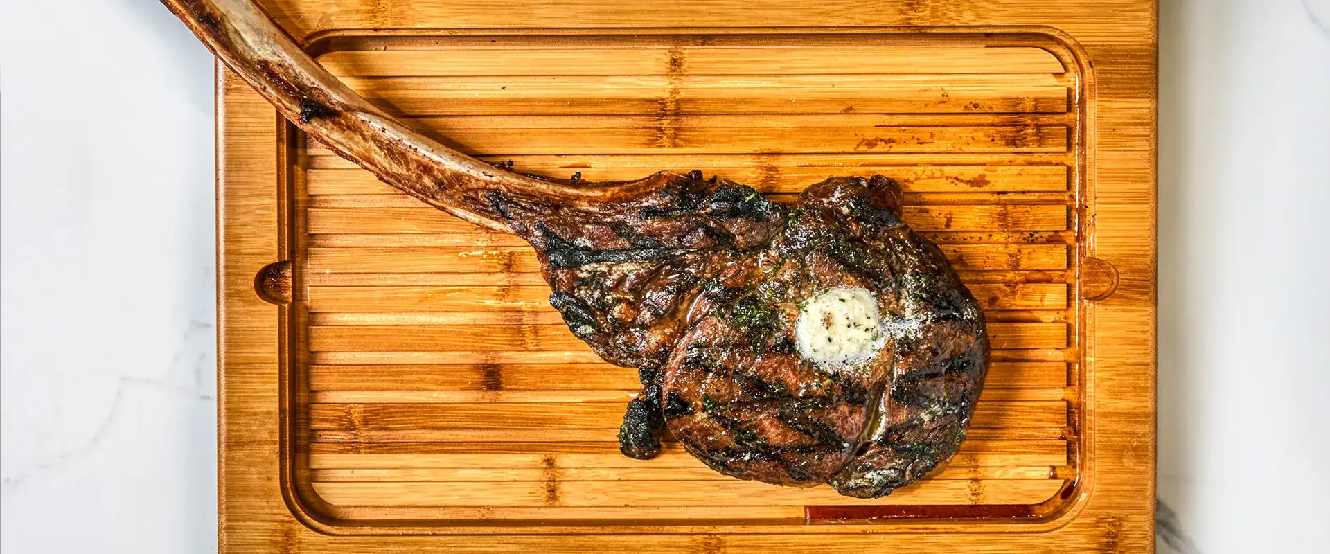 Tomahawk steak with compound butter on a wooden board.