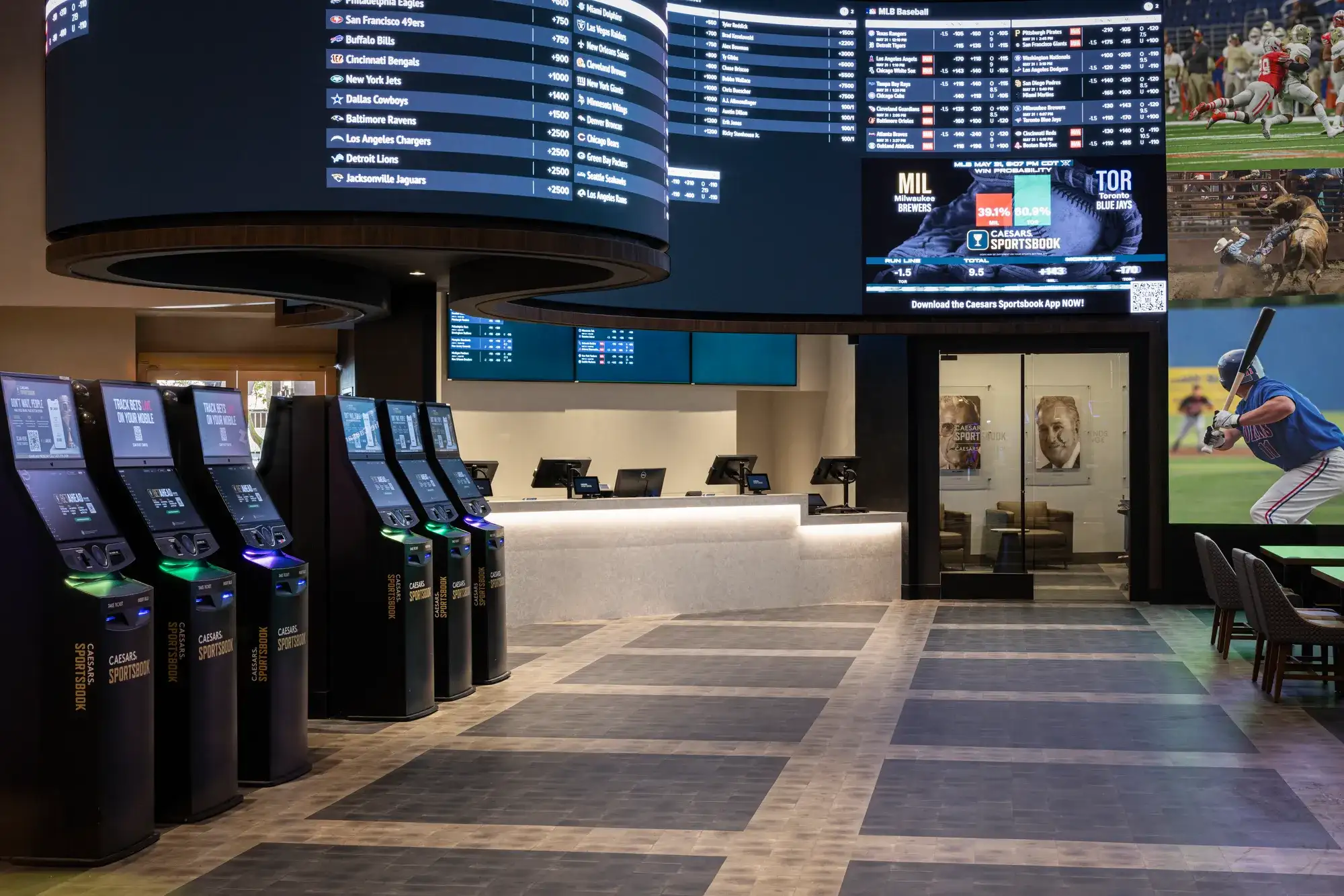 Caesars Sportsbook interior with betting kiosks, odds boards, and large screens showing baseball and other sports