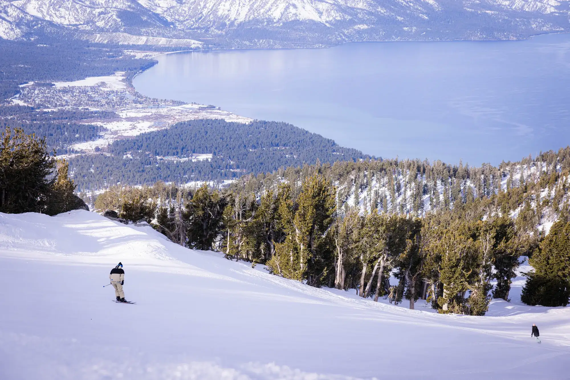 Snow-covered ski slope above South Lake Tahoe with lake views, evergreen trees, and snowy mountain peaks in winter