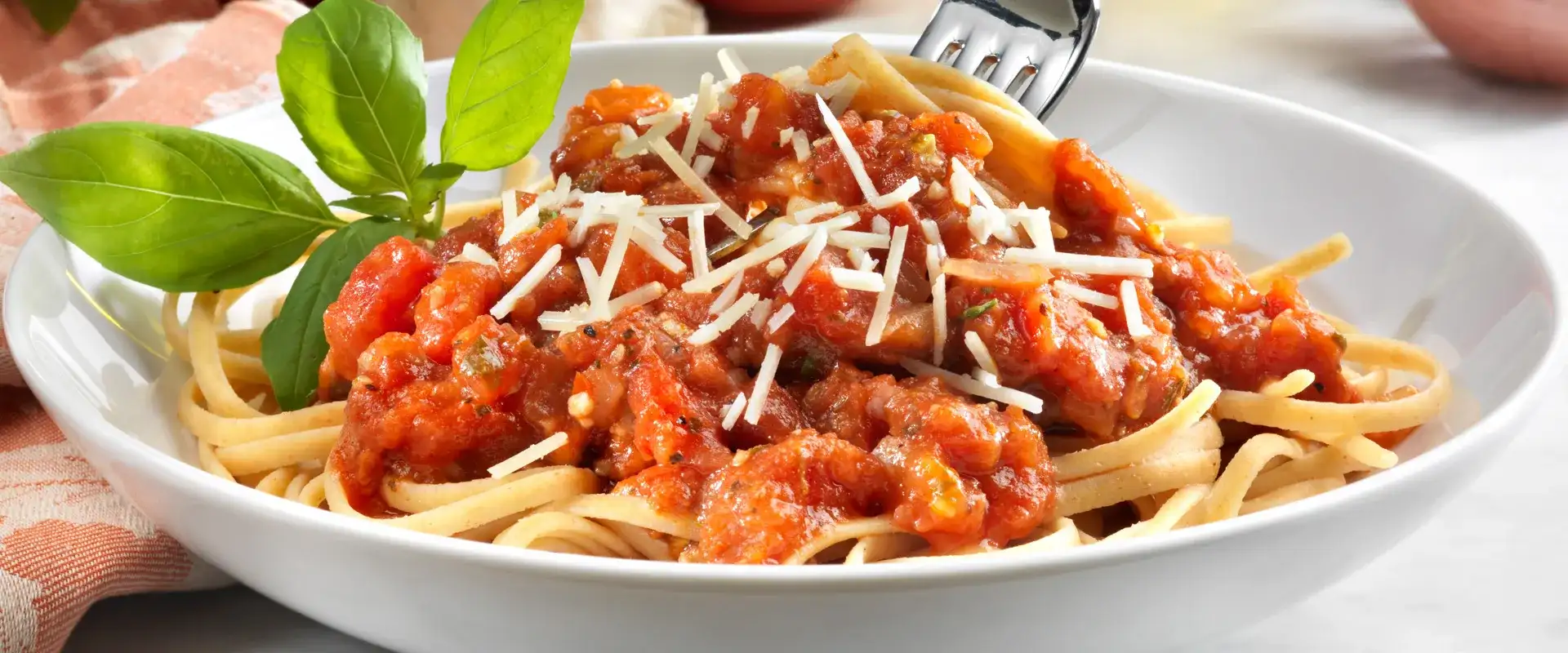 Bowl of linguini with marinara and topped with shredded Parmesan and fresh basil.