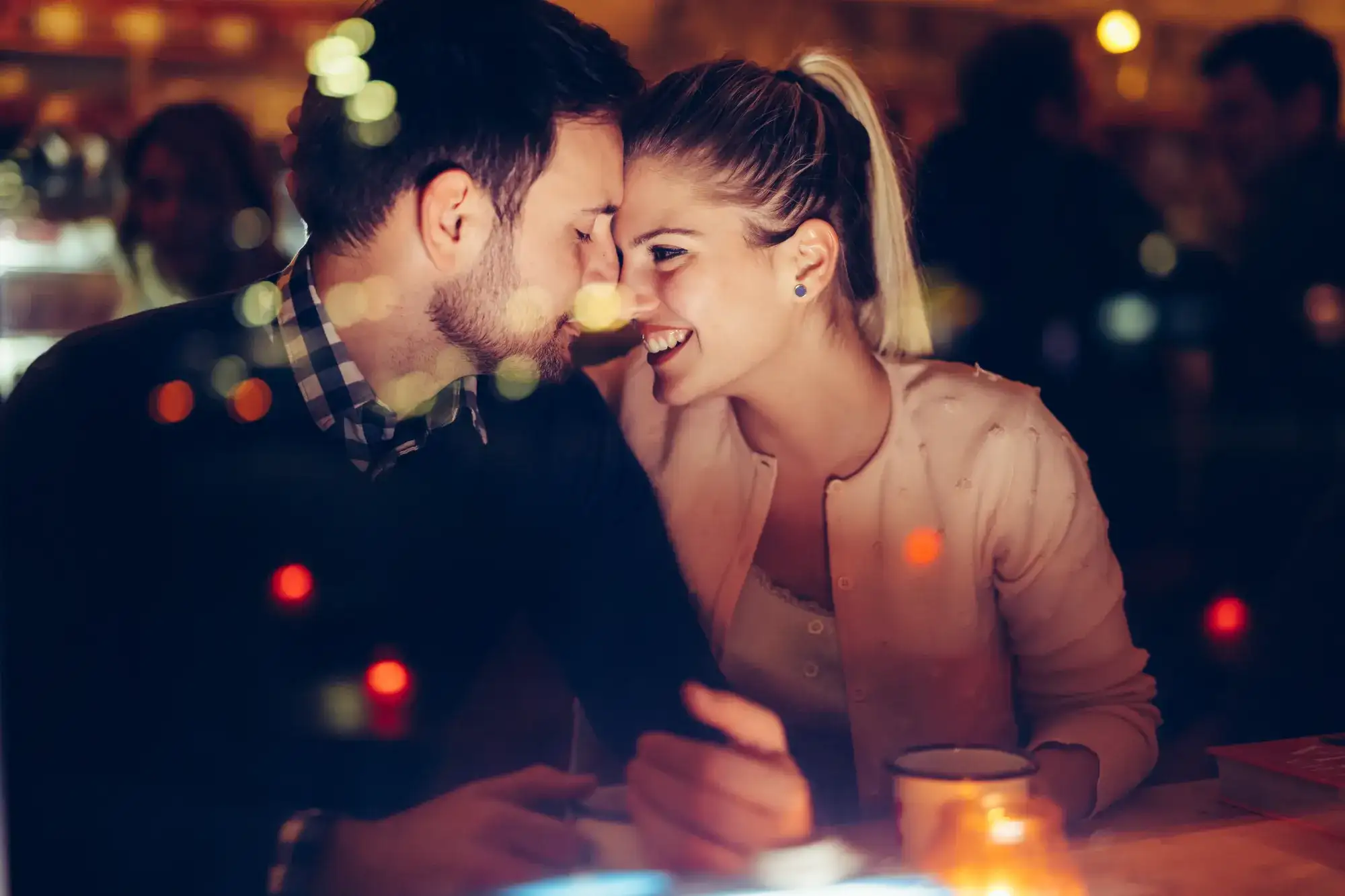 Two people seated closely at a candlelit restaurant table with a drink, capturing a romantic Vegas anniversary dinner atmosphere.