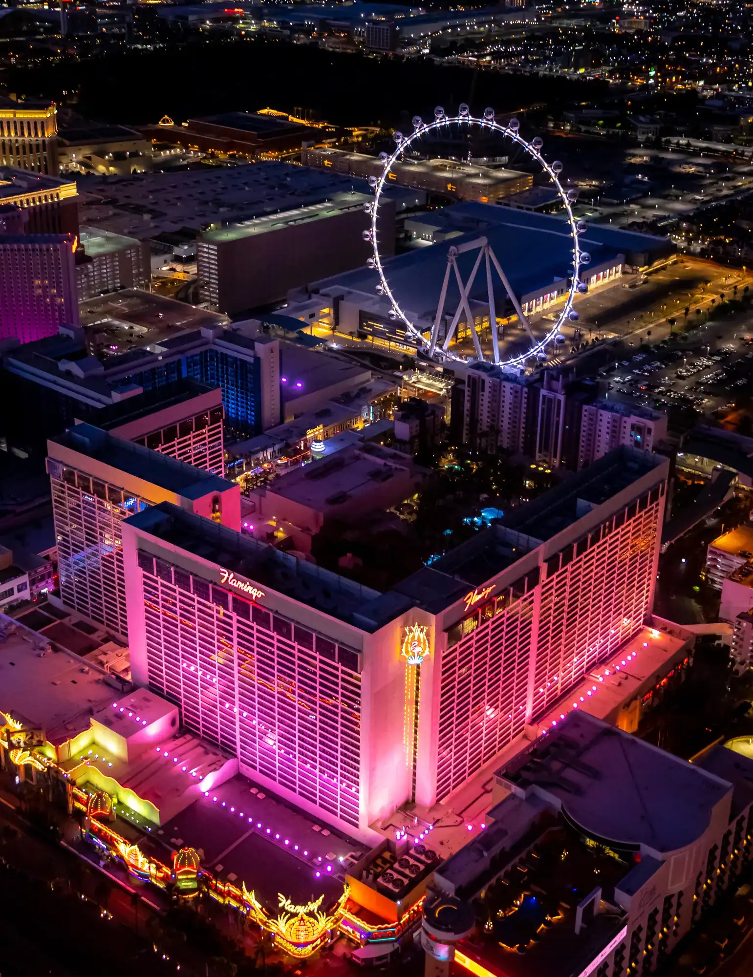 Aerial view of Flamingo Las Vegas at night with pink-lit towers, neon signage, and Center Strip lights