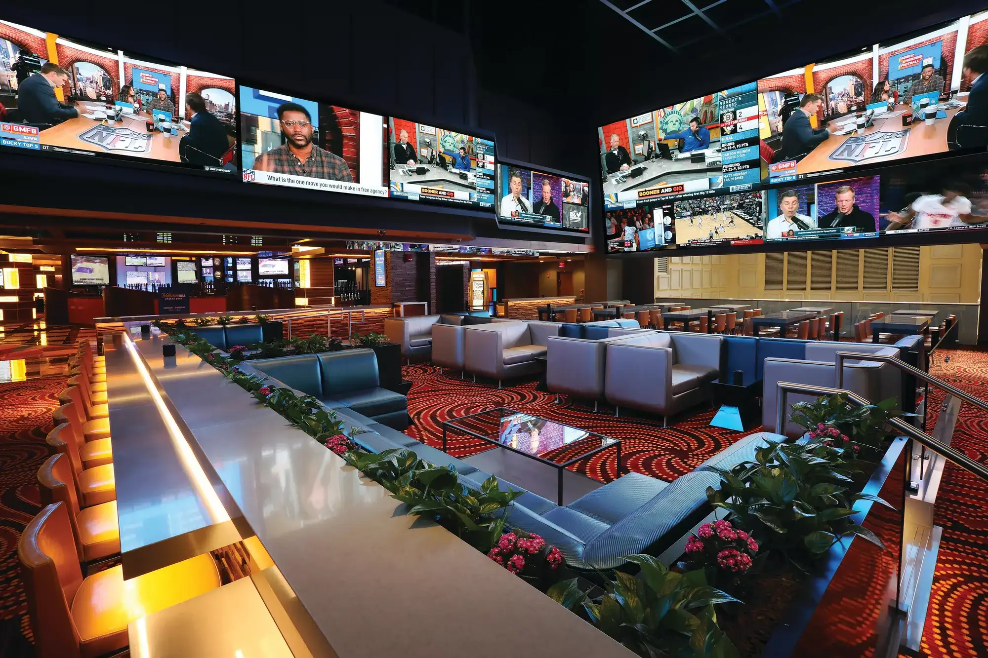 Caesars Sportsbook lounge with bar seating and large video screens showing sports broadcasts