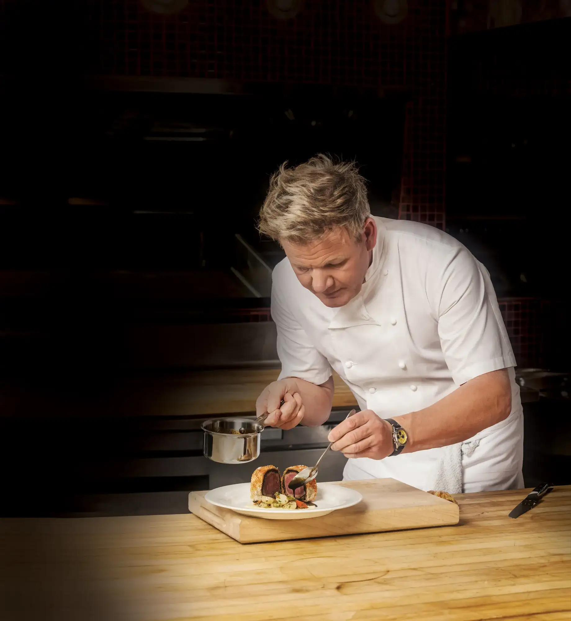 Gordon Ramsay adding sauce to sliced beef Wellington on a plate in a professional kitchen