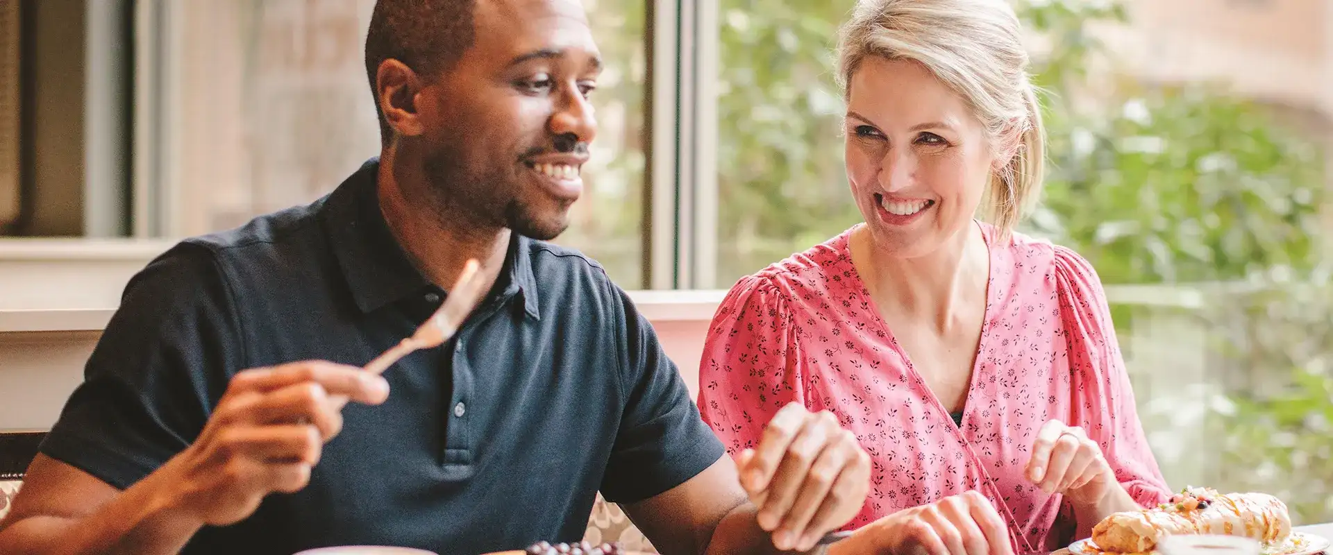 Two people enjoying a meal by a large window.