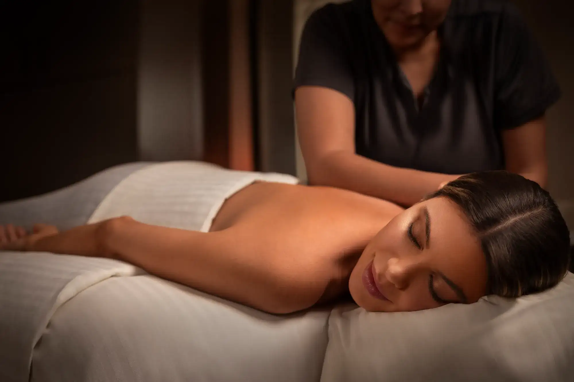 Spa therapist providing a back massage to a woman resting on a padded treatment table