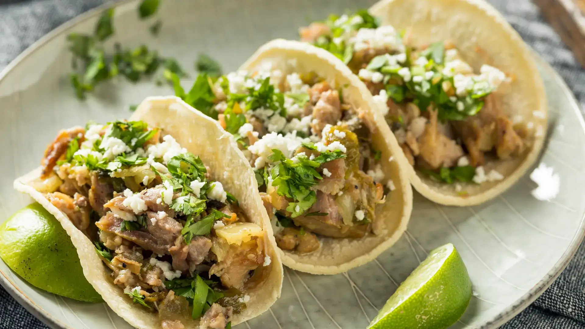 Three soft tacos on a plate with lime wedges.