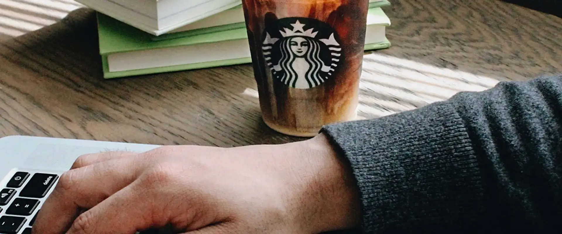 Person using laptop with a Starbuck's beverage.