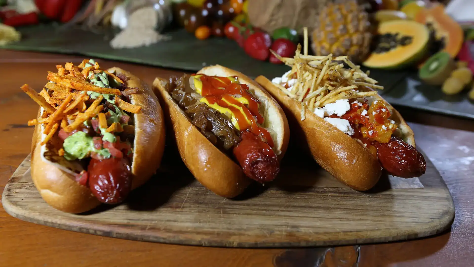 Three gourmet hotdogs on a wooden platter.
