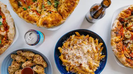 Pizzas, wings, and French fries in dishes on a table with beers.