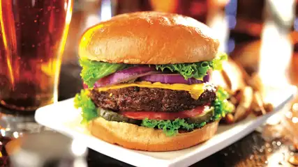 Cheeseburger with lettuce, onion, tomato, and a pint of beer.